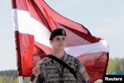 Латвийский солдат держит национальный флаг в ожидании прибытия десантников 173-й пехотной бригады армии США, базирующейся в Италии. Аэропорт Риги, 24 апреля 2014 года, фото Reuters